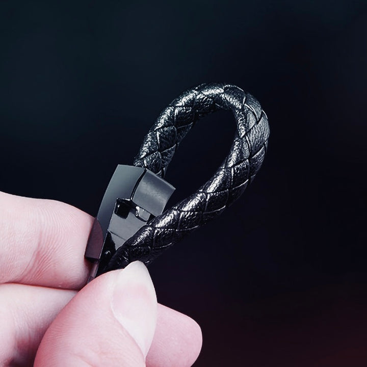 Black braided leather keychain held by a hand against a dark background